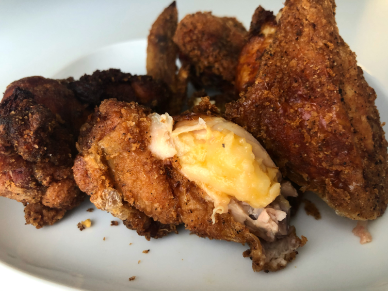 On a white plate, there is a fried chicken wing with orange cheesy macaroni under the skin. Photo by Alyssa Buckley.