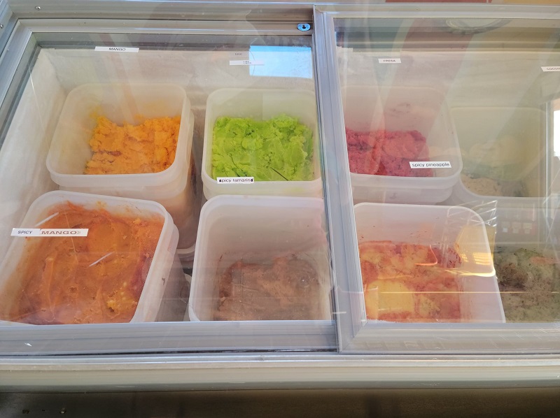 A display case of water-based ice cream with mango, spicy mango, spicy tamarind, and spicy pineapple seen most clearly. Photo by Matthew Macomber.