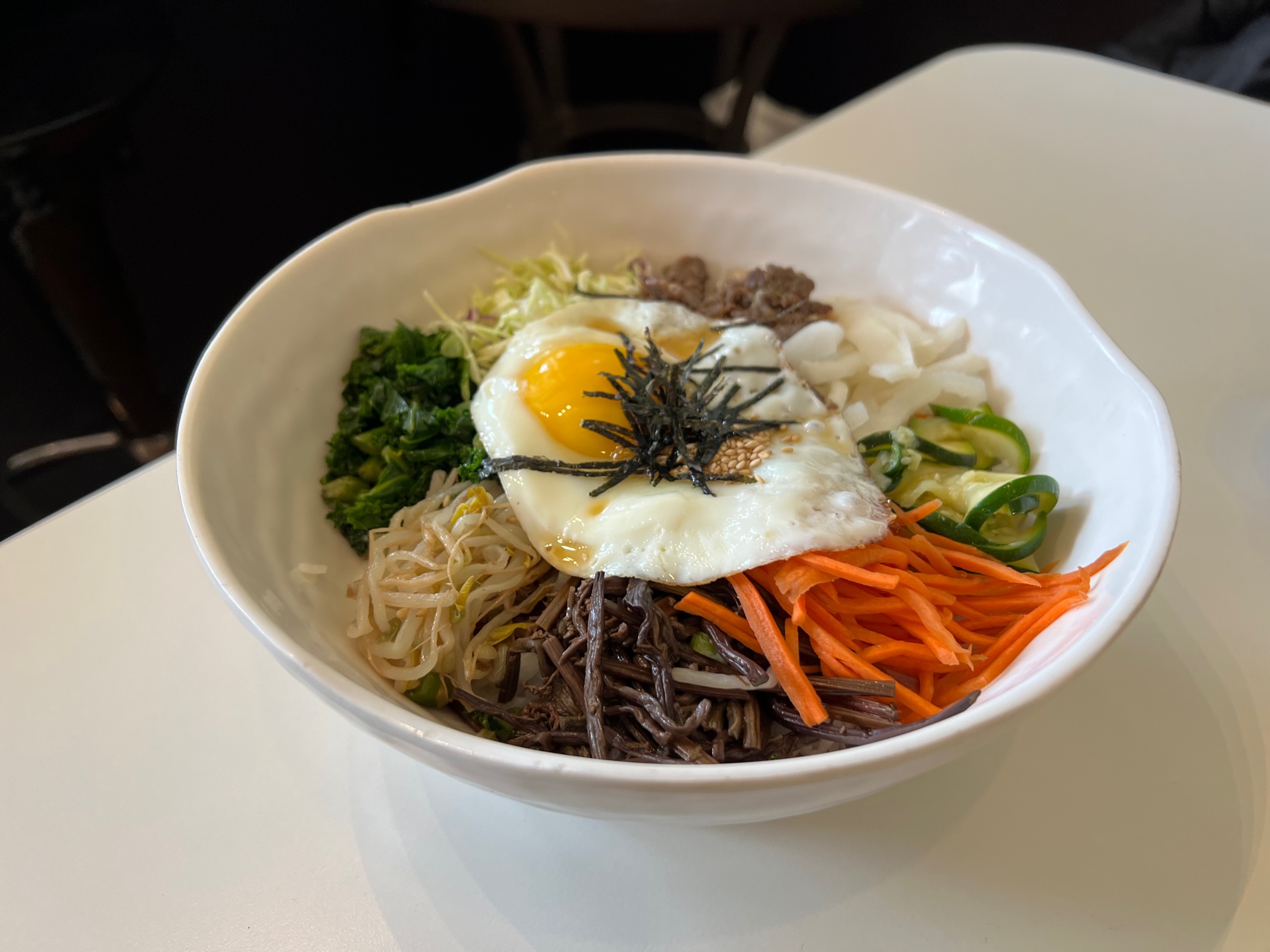On a white table, there is a bowl of bibimbap from San Maru in Champaign. The fried egg is cooked perfectly and centered atop different vegetables. Photo by Alyssa Buckley.