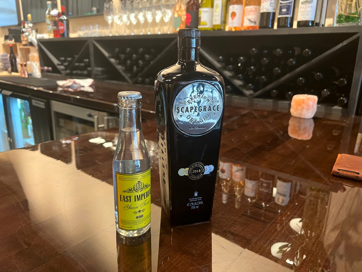 Inside Ladro Enoteca in Downtown Champaign, there are two bottles on the dark wooden counter. The left bottle is a small, clear. bottle of tonic, and the right bottle is a larger dark blue bottle of Scapegrace gin. Photo by Alyssa Buckley.