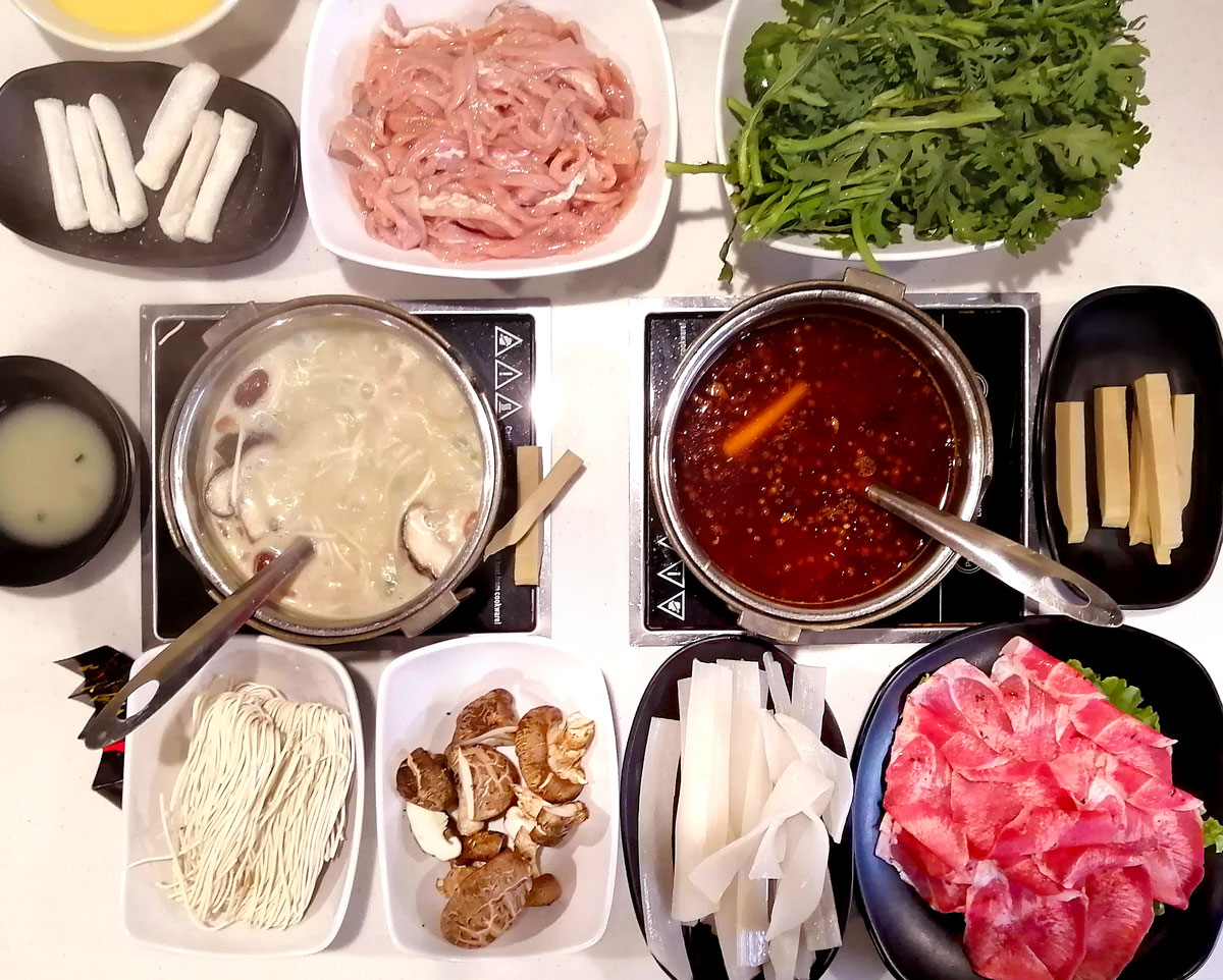 An overhead view of various raw ingredients ready to to cook in the two pots of broth sitting top of a table. Photo by Paul Young.