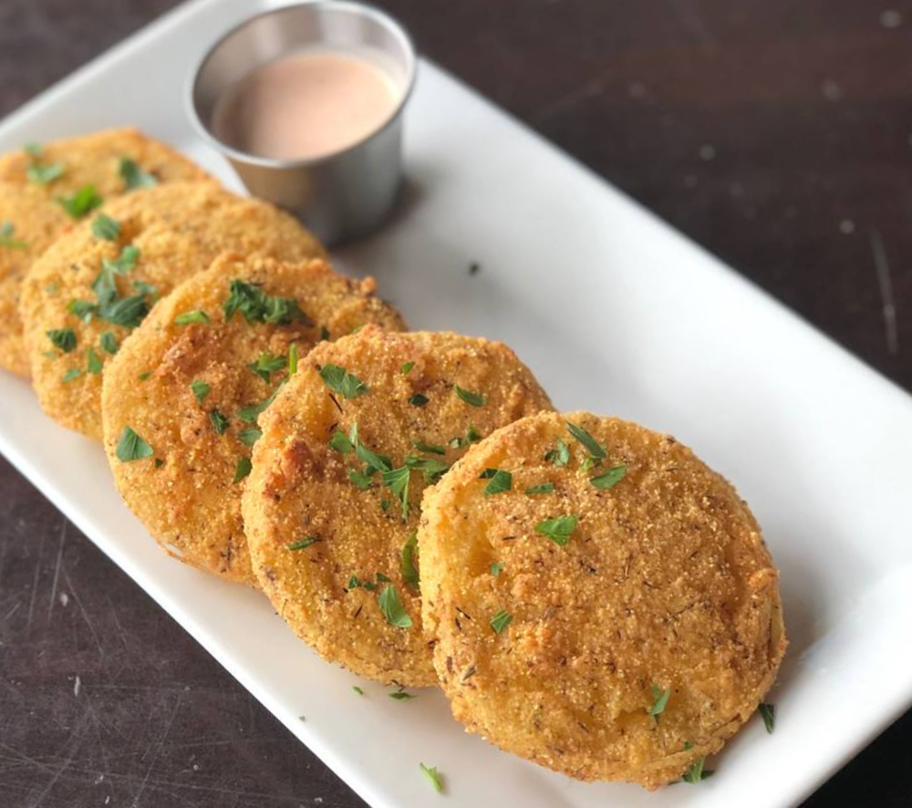On a white plate, there are several fried green tomatoes with a perfectly golden exterior flecked with freshly chopped parsley. Photo by Jessica Hammie.