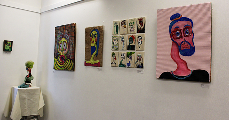A series of paintings and sculptures covering two walls. 