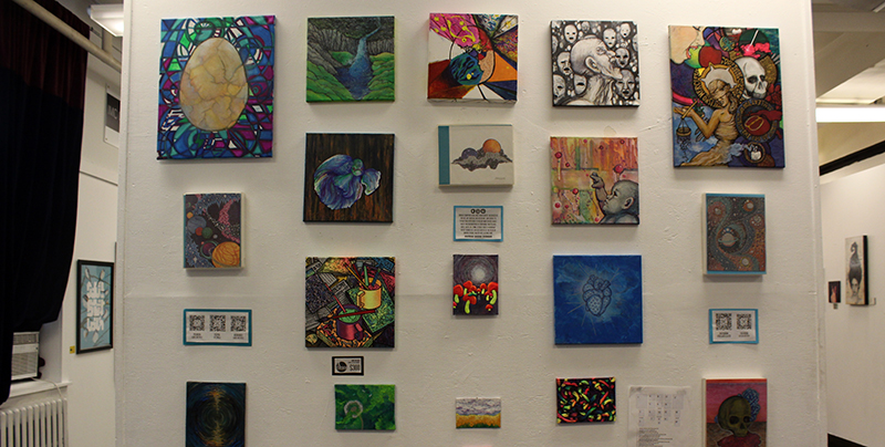 A series of multicolored, multi-size painting on center wall with other work on the right and left side walls. 