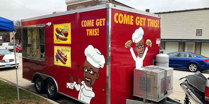 Outside in Champaign, Illinois, there is a red food truck with photos of food, a bitmoji of the chef, and the truck's name 