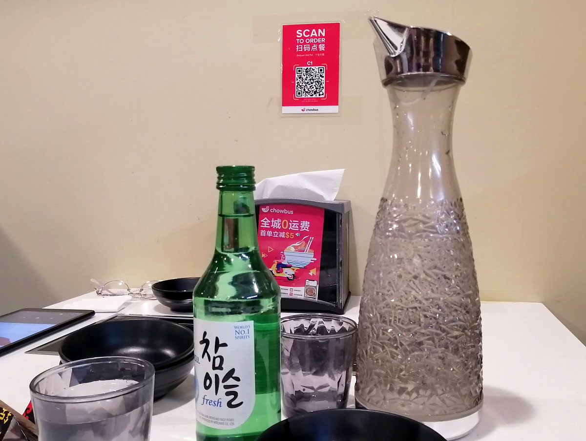 A picture showing a sign with a QR code and a botte of soju sitting on a table. Photo by Paul Young.