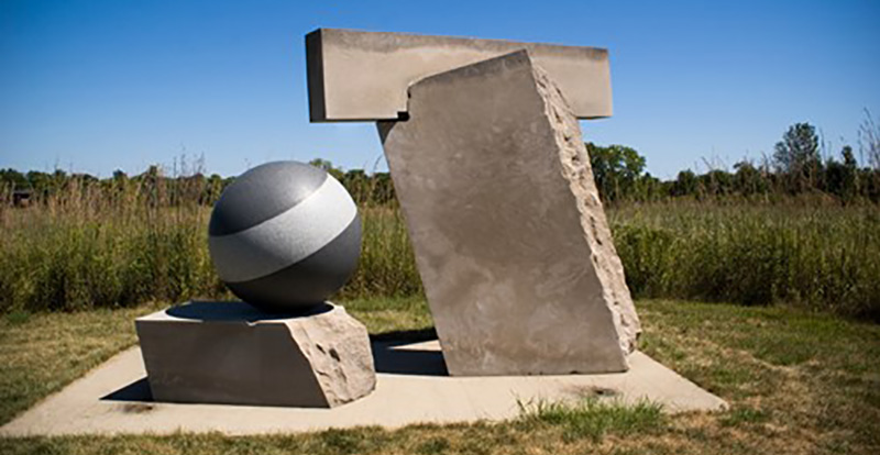Photo of sculpture with cement striped globe and t-shaped blocks at Wandell Sculpture Garden at Meadowbrook Park.
