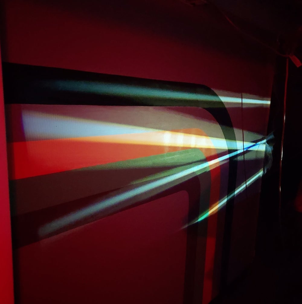 Projection lights up a wall, colors streak across the wall. 