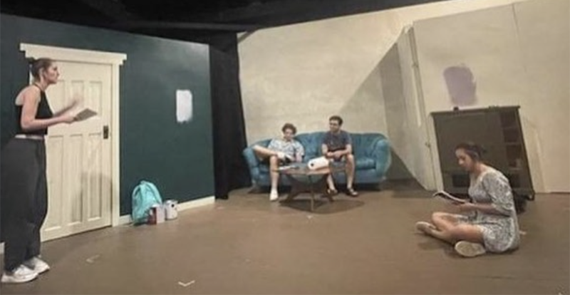 Photo of rehearsal for Bad Jews at the Station Theatre two women, one on left, one on right, talking to two men who are seated on a couch across the room. 