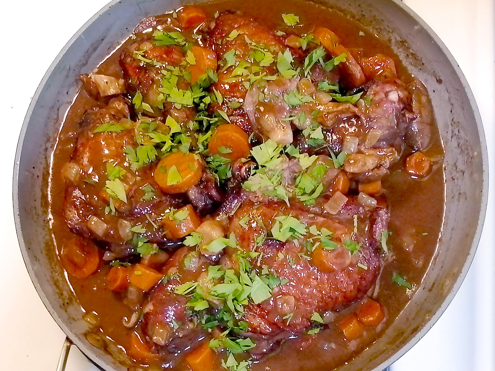 A skillet containing chicken, mushrooms, and carrots in a rich red wine sauce garnished with chopped parsley. Photo by Paul Young. 