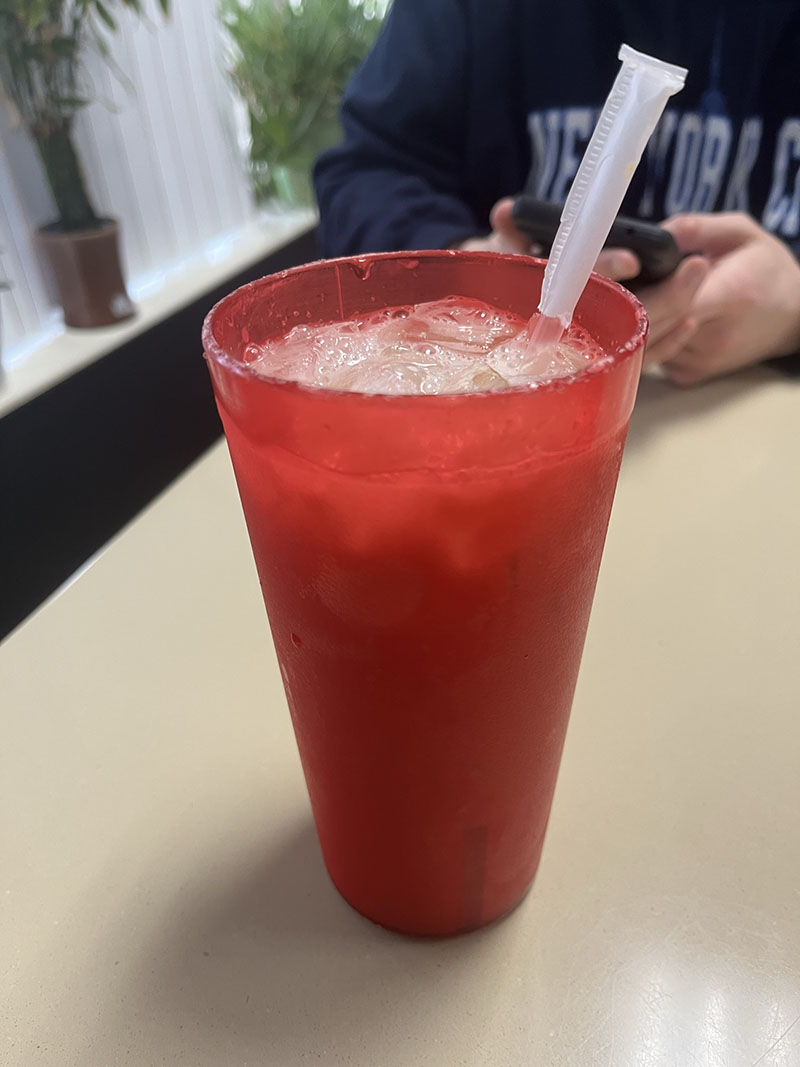 A tall, red plastic cup filled with ice and a white liquid sits on a beige table. A straw with a paper wrapping pokes up from the top of the cup. Photo by Julia Freeman.