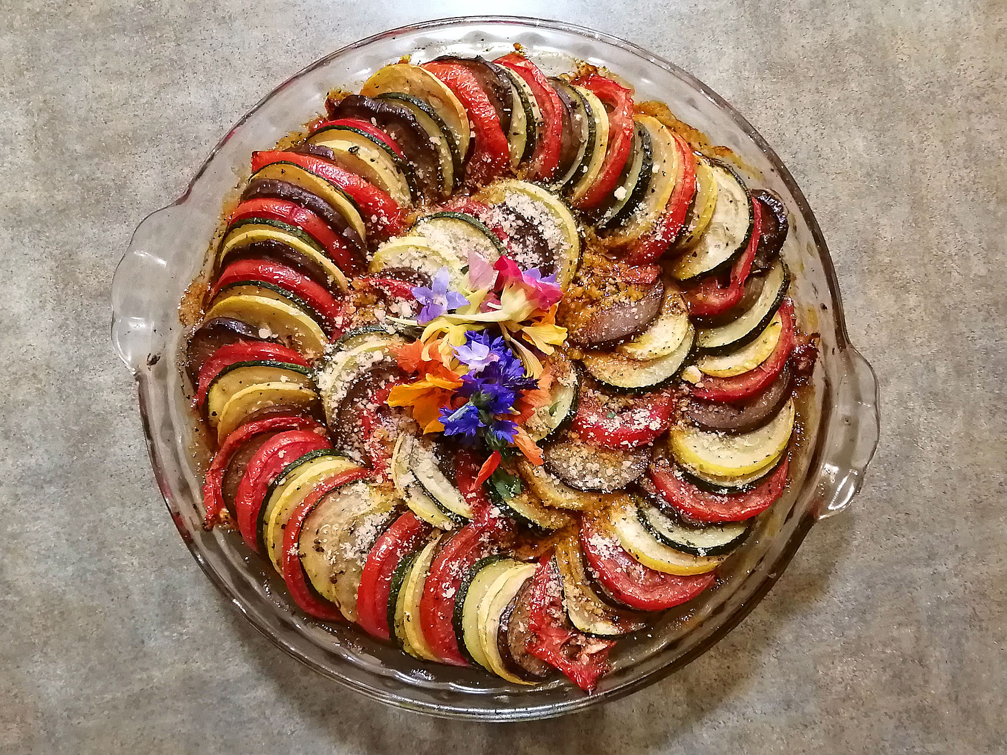 A round baking dish with an arrangement of grilled vegetable slices in many colors garnished with some edible flowers. Photo by Paul Young.