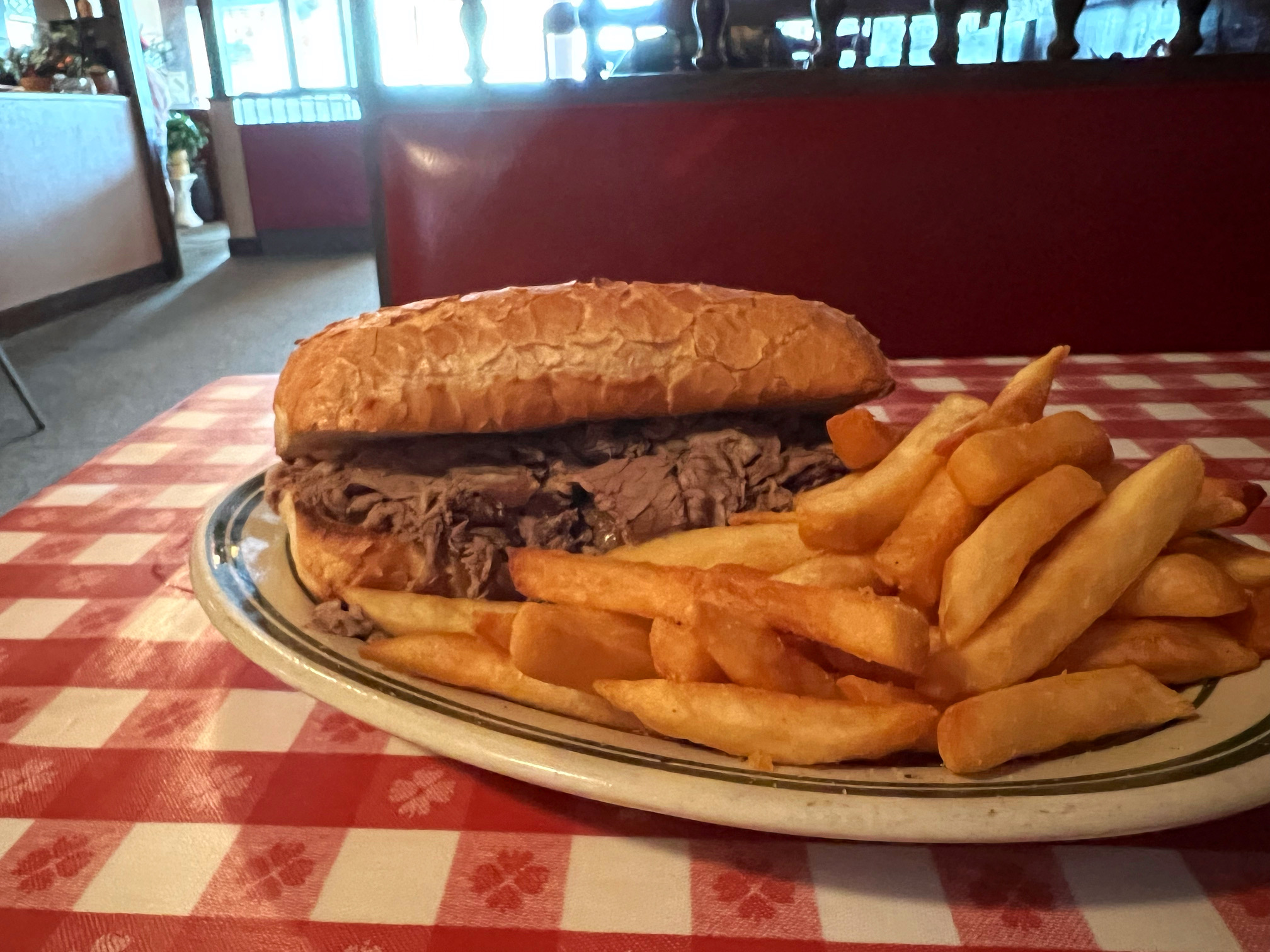 On a red-and-white checkered tablecloth, there is an oval plate with an Italian beef and fries on it. Photo by Alyssa Buckley.