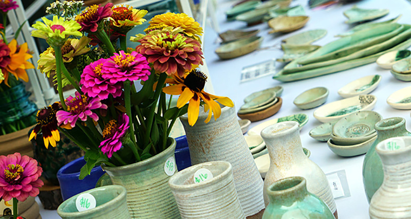 A selection of ceramic cups, pots, and vases, including one vase with brightly colored floweres.