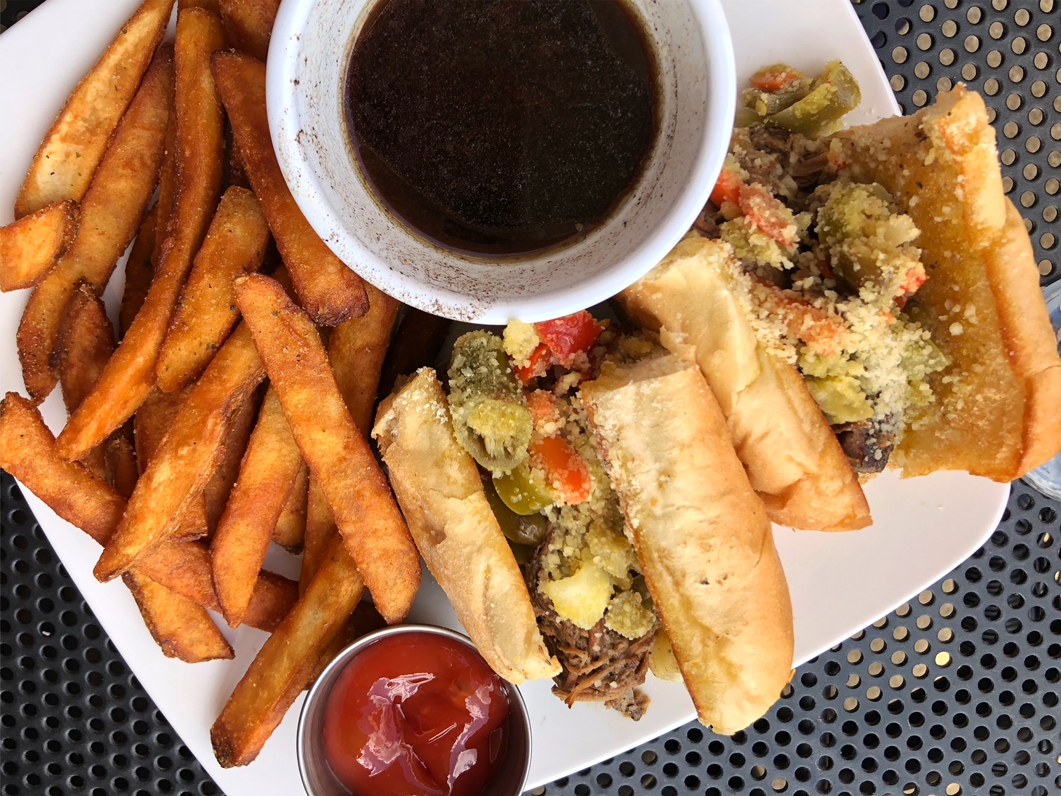On Baxter's American Grille's outdoor patio in Champaign, there is a plate with a sliced Italian beef with pepeprs and Parmesan plus a side of seasoned fries anda cup of ketchup and cup of au jus. Photo by Alyssa Buckley.