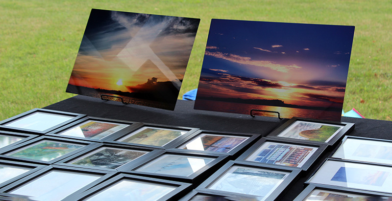 A display of photos on a table outside on the grass. In the foreground are two skyscapes.