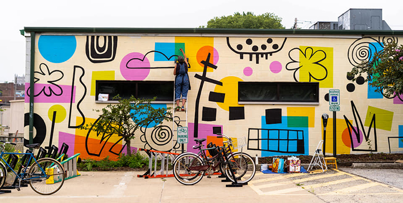 Wide shot of Lisa Kesler's Summer Rhythm mural at 25 O'Clock featuring black outlines in abstract and geometric shapes and brightly colored shapes in yellow, magenta and cyan. 