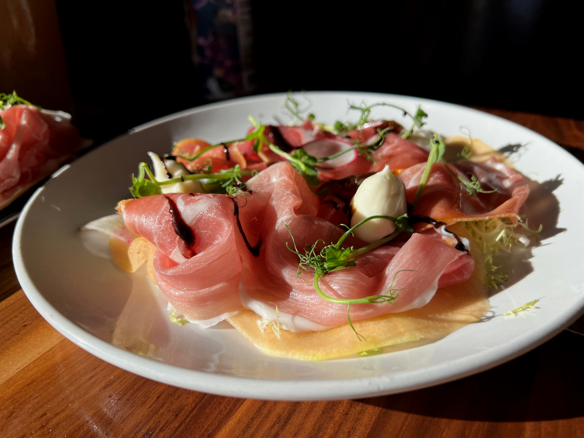 On a white plate, there is proscuitto with cantaloupe, balsamic glaze, white soft cheese, and frisee. Photo by Alyssa Buckley.