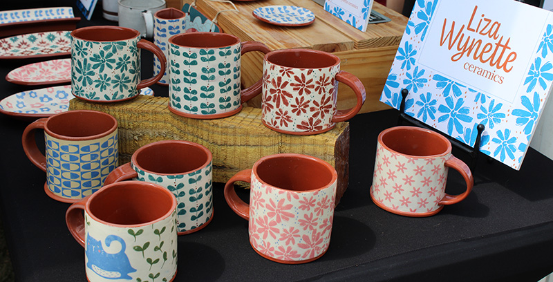 A display of red clay mugs, bowls and plates with delicate floral designs.