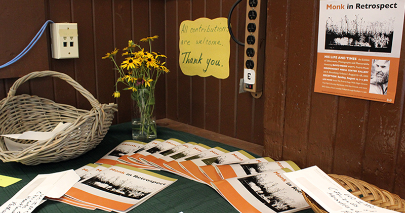 Table against a paneled wall with copies of exhibit programs and donation baskets and vases of Black-eyed Susans. 