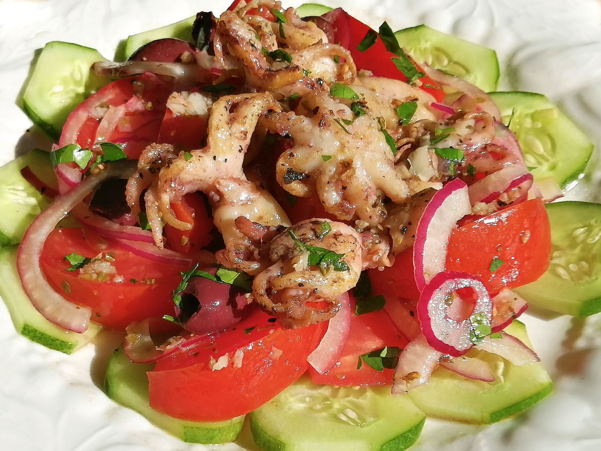 A white plate topped with dressed cucumbers, tomatoes, red onion, and olives; several grilled baby octopi are layered on top. Photo by Paul Young.