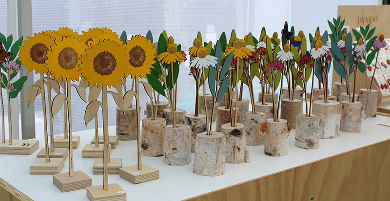 A display of handpainted wooden sunflowers and other flowers against a white cloth.