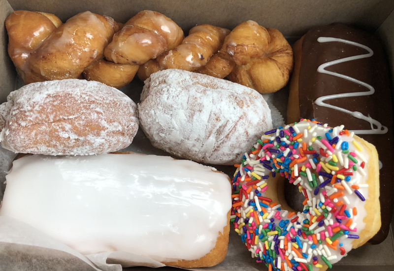 A box of doughnuts from Royal Donuts in Danville. Included in the box are twisted, glazed ones, a long john with white icing, a round doughnut with sprinkles, and two powdered ones.