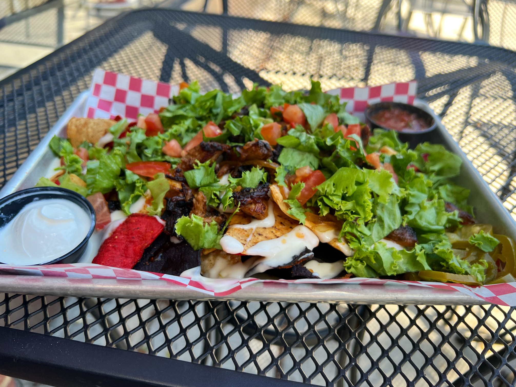 On a black outdoor table, there is a tray of nachos with tricolor chips topped with lots of romaine. Photo by Alyssa Buckley.