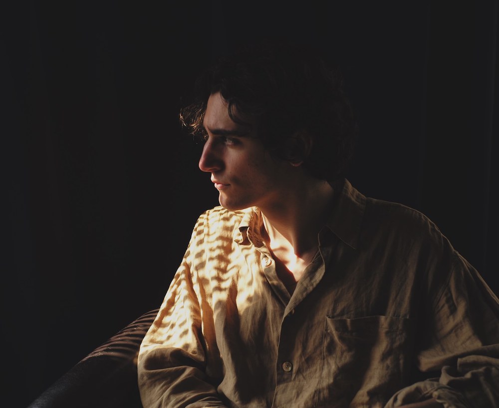 Singer Tamino looks to the left in front of a black background, a single light shines on the singer.