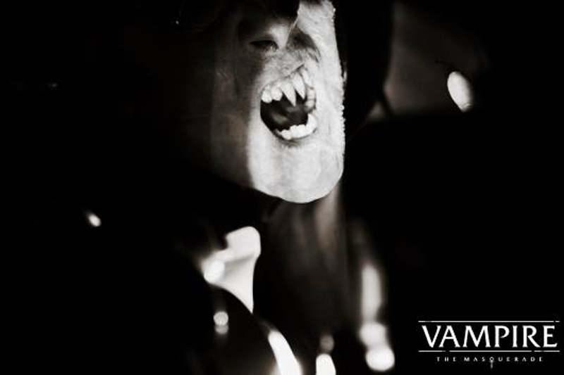 Dramatically lit black and white photo of what appears to be a vampireâ€™s face, though the top of the head and eyes are cloaked. The mouth is open and fangs are present. The bottom right of the image has text that reads, â€œVampire the Masquerade.â€ Photo from the Facebook event page.