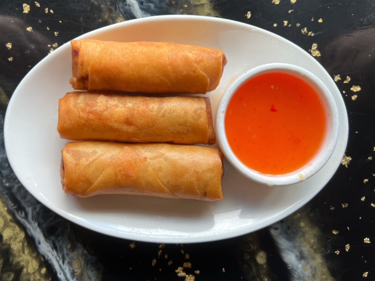 On a white oval plate at Sticky Rice in Champaign, there are three golden pork spring rolls. Photo by Alyssa Buckley.