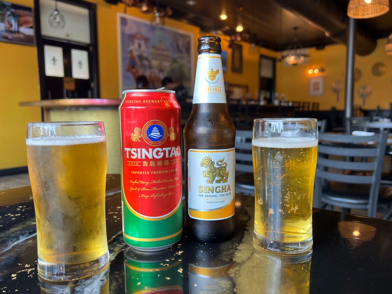 On a black table inside Sticky Rice in Champaign, Illinois, there are two beers with two glasses of filled lager with a light head. Photo by Alyssa Buckley.