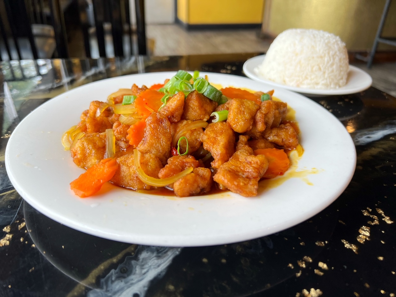 On a black table, there is a white plate with Sticky Rice's General Tso's chicken with carrots. Photo by Alyssa Buckley.