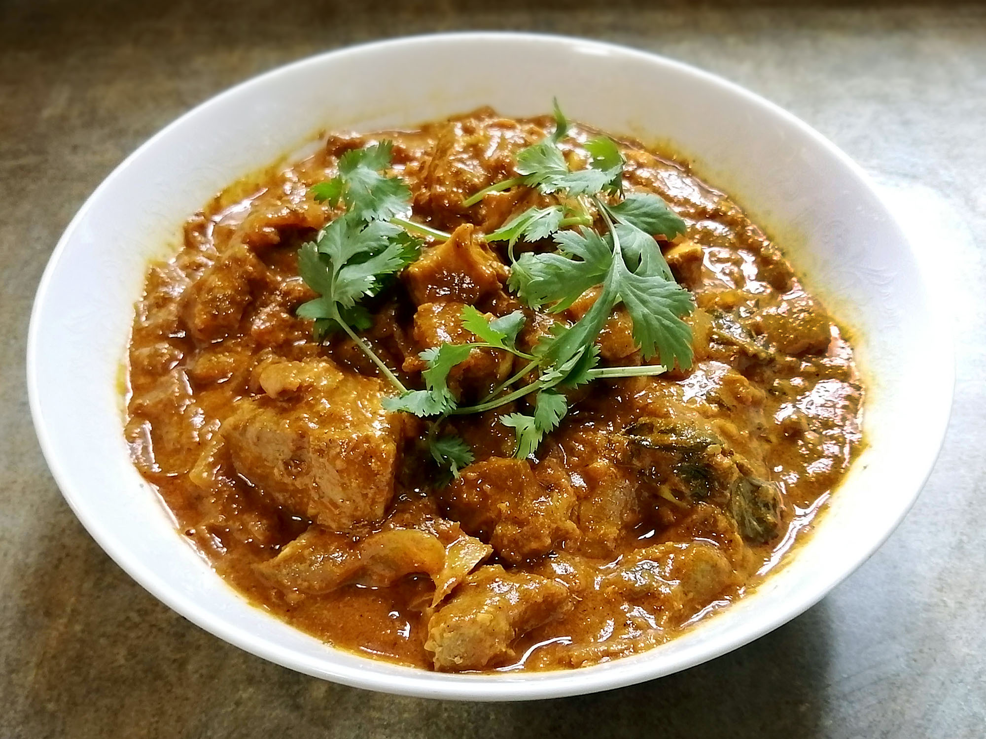 A large bowl of goat meat in a orange-brown curry sauce garnished with cilantro leaves. Photo by Paul Young.