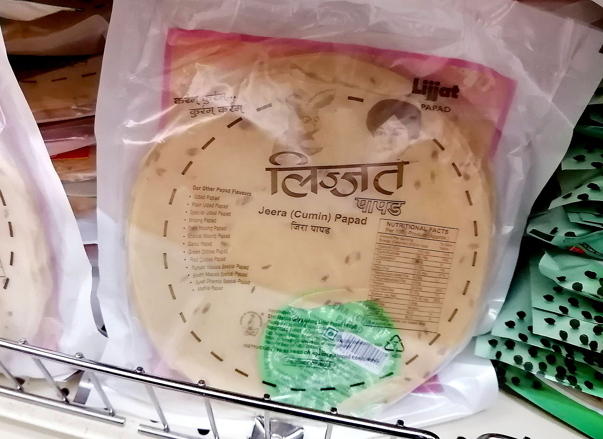 A package of uncooked round crackers labeled â€œJeera (Cumin) Papadâ€ on a shelf with other products. Photo by Paul Young.