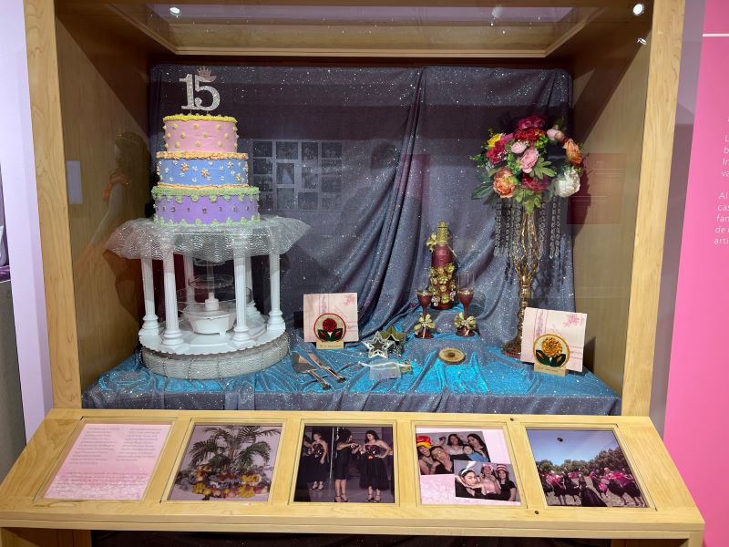 A display case with a tiered cake, floral bouquet, decorated champagne bottle and glasses, and other items. Photo by Julie McClure.