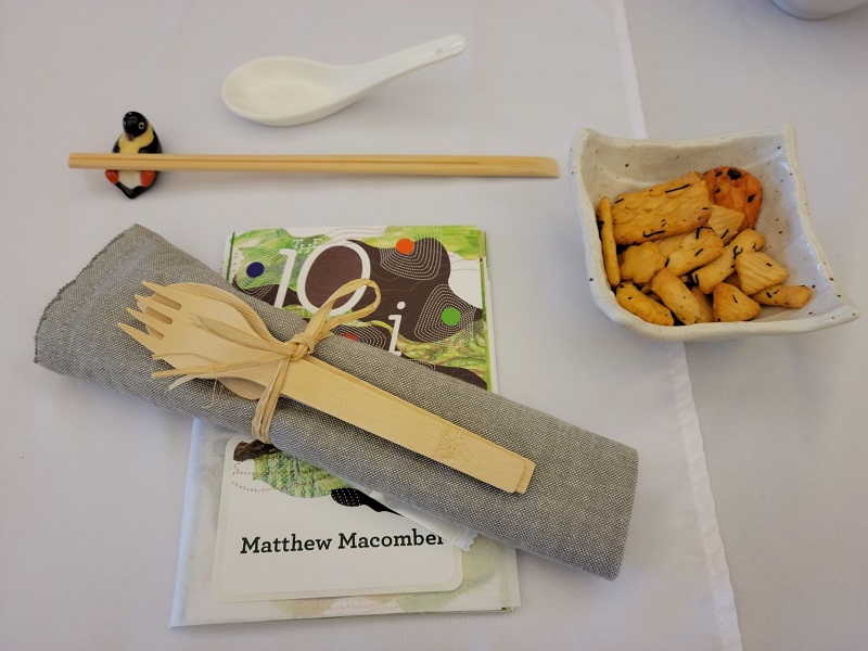 A table setting with a penguin chopstick holder, rice cracker in a small bowl, wooden utensil, cloth napkin, and a pamphlet of the food and chefs for the night. Photo by Matthew Macomber.