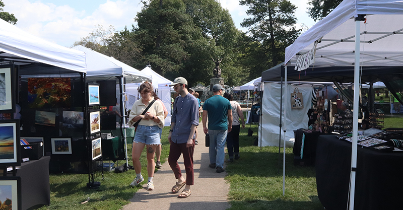 Photo of people walking through West Side Park looking at the various art tents.