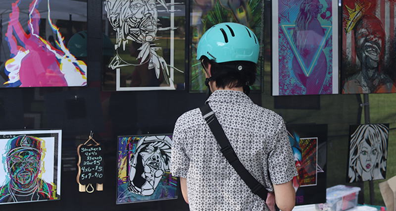 A visitor with a bike helmet looking at a variety of illustrated prints hanging on the inside wall of a tent.