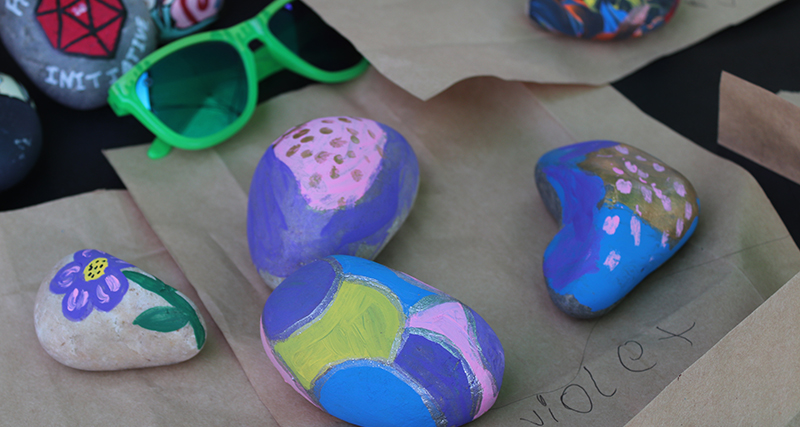 A group of colorfully painted rocks and fluorescent sunglasses on brown craft paper.