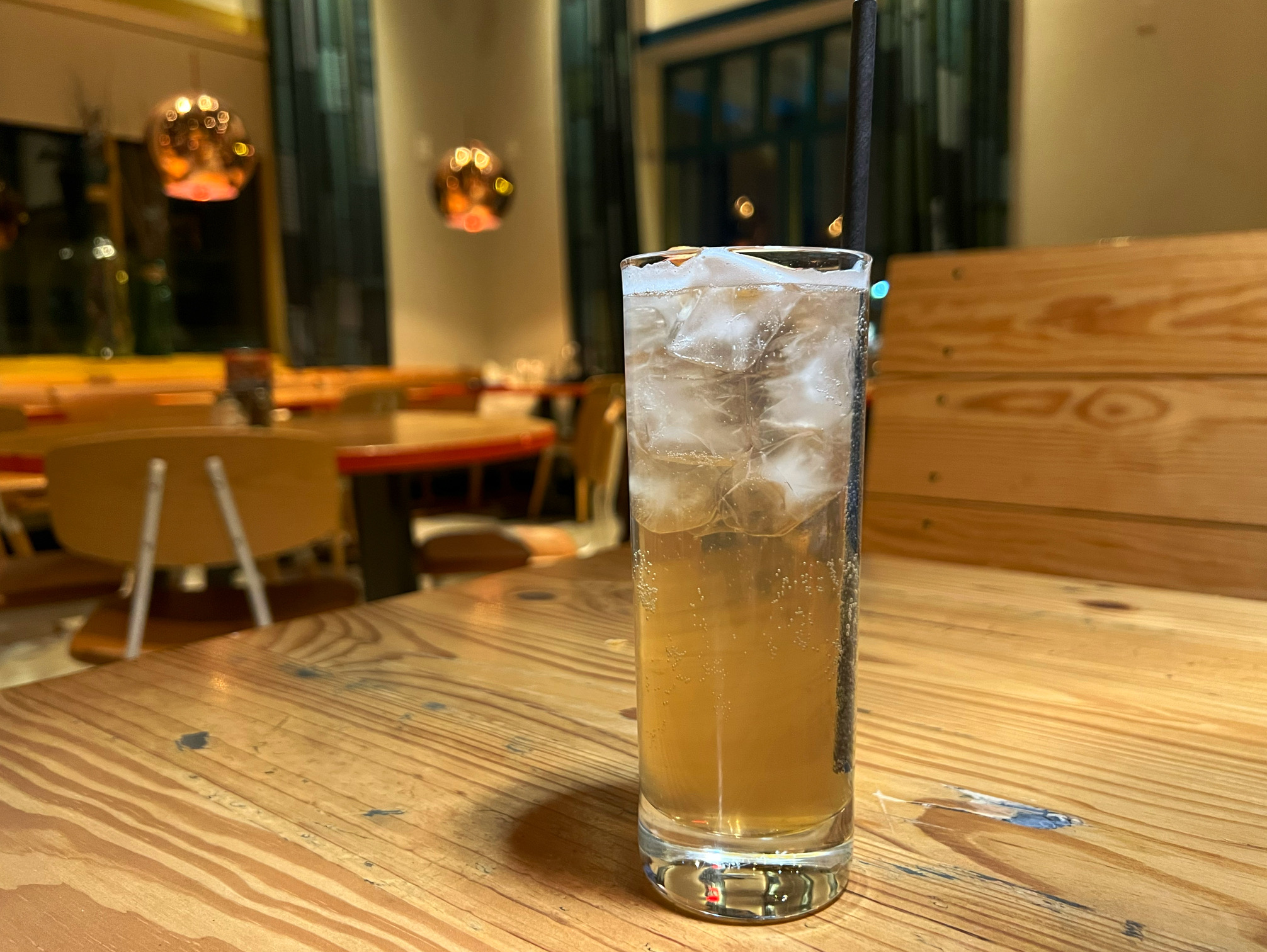 On a wooden table, there is a tall skinny glass with a light brown drink . Photo by Alyssa Buckley.