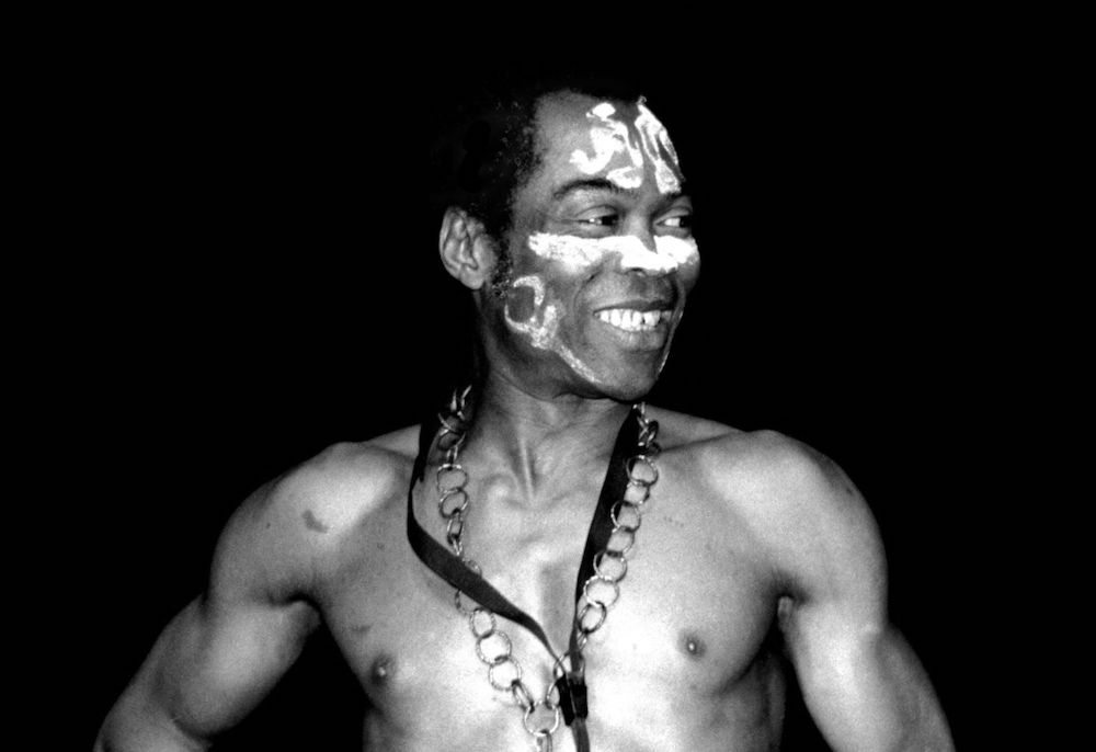 Black and white portrait of Fela Kuti. He looks off to his left and smiles.