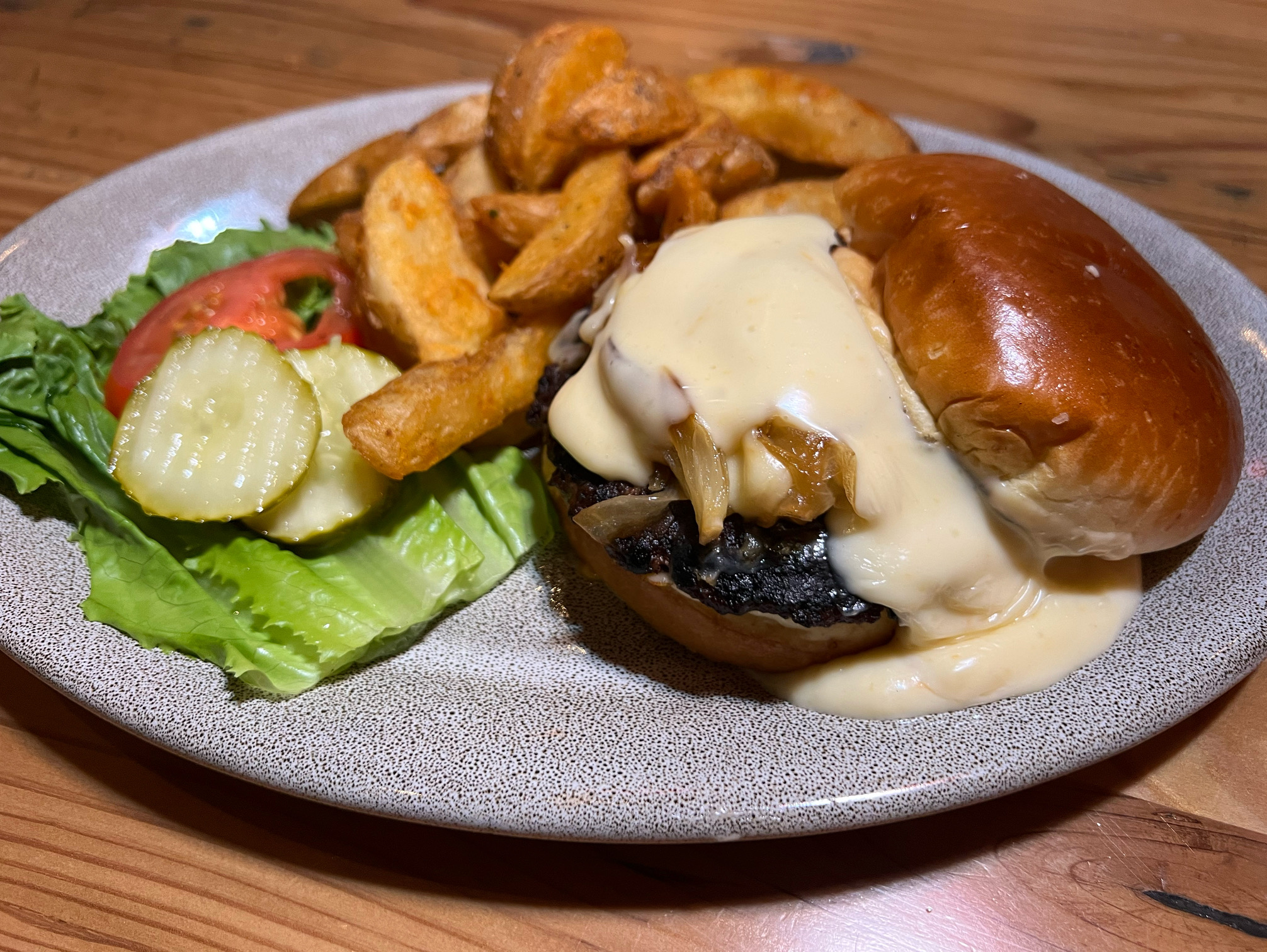 On a gray speckled plate, there is a burger drowning in housemade cheese sauce with a side of fries. Photo by Alyssa Buckley.