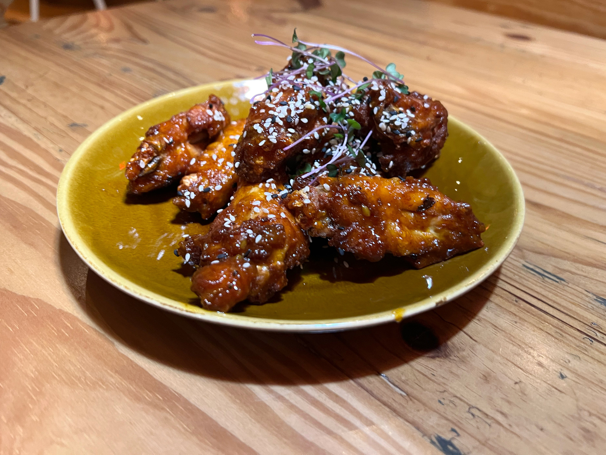 On a greenish-yellow plate there is an order of eight chicken wings prinkled with sesame seeds and microgreens. Photo by Alyssa Buckley.