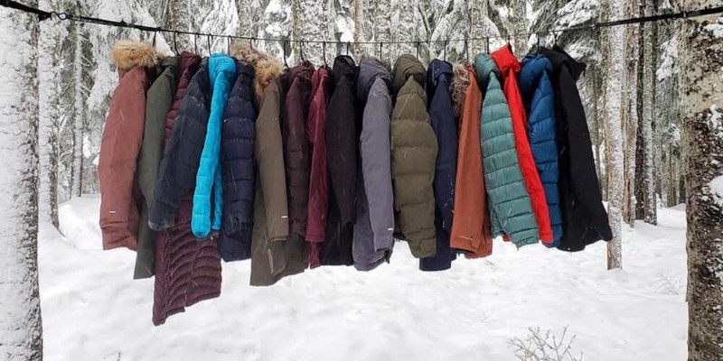 Winter coats hanging on a clothesline. The ground is covered in snow.
