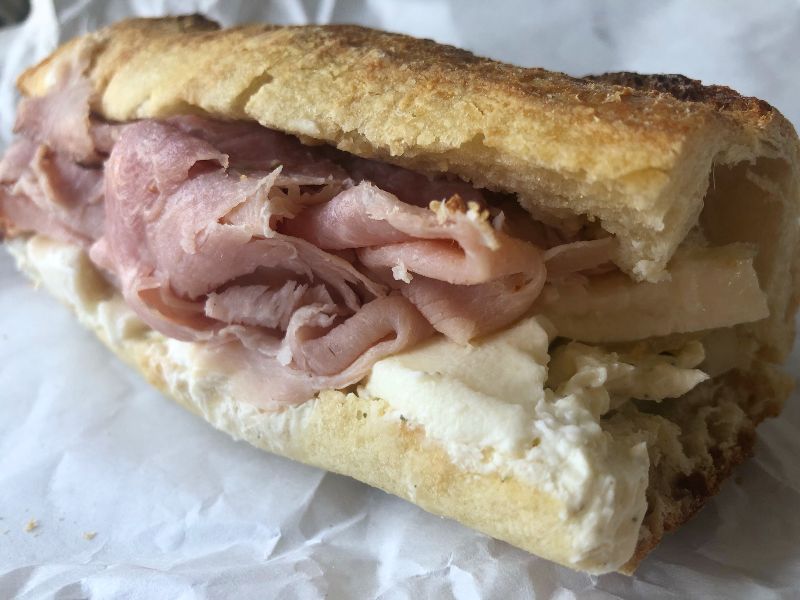 On white parchment paper, a sandwich called Frankensandwich from Cheese & Crackers is uncut and uneaten. Photo by Alyssa Buckley.