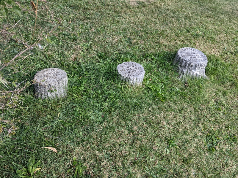 Three small headstones shaped like tree stumps are in a row. Photo by Tom Ackerman.