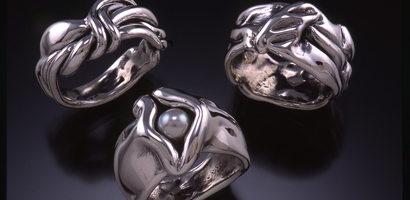 three silver handcrafted rings with organic twists and curves against a black background.