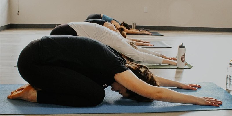 A yoga class where a row of people are seated on mats and bent forward with foreheads touching the mats.