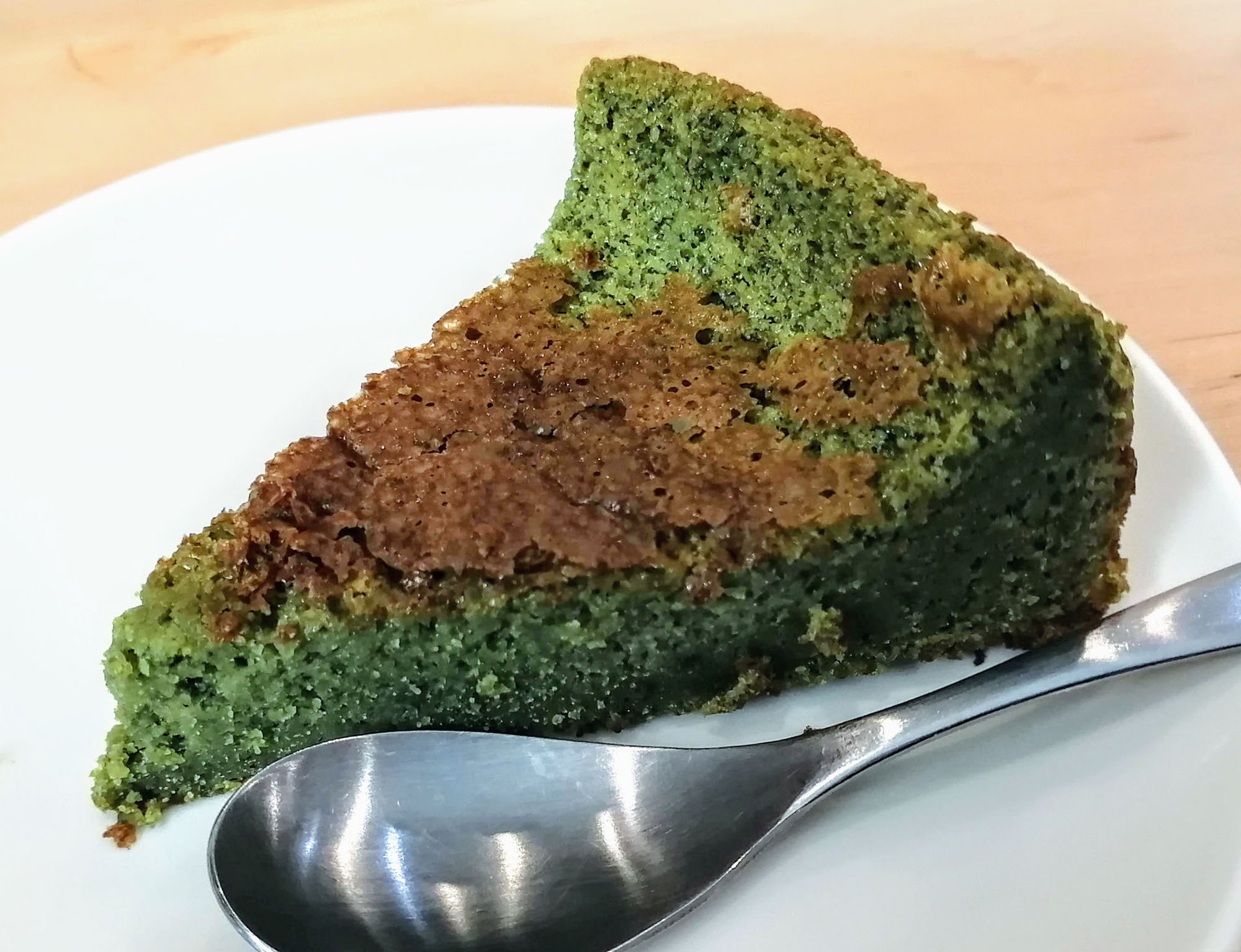  A close-up of a triangular slice of green and brown cake on a white plate with a spoon. Photo by Paul Young.